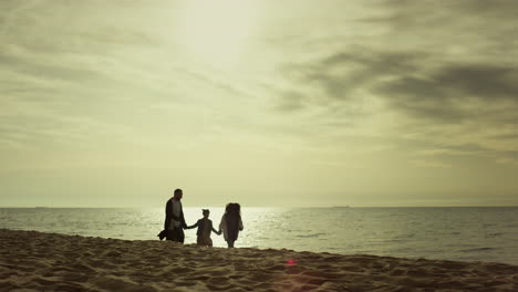 Eltern-Kinder-Laufen-An-Der-Küste.-Eine-Kleine-Familie-Genießt-Einen-Spaziergang-Am-Strand-Bei-Sonnenuntergang.