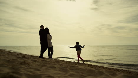Family-relaxing-beach-vacation.-Parents-looking-kid-playing-at-morning-sea-shore