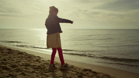 Happy-kid-playing-alone-on-sea-beach.-Young-girl-have-fun-on-morning-ocean-shore