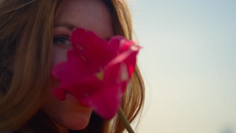 Closeup-beautiful-woman-face-enjoying-tulip-flower-in-soft-sunset-light-outdoor.