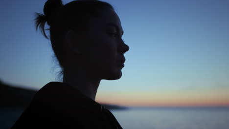 Dark-silhouette-face-woman-standing-in-front-evening-sky-close-up.-Girl-relaxing