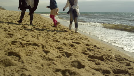 Family-legs-play-beach-together-at-sea-shore.-Fun-people-walking-by-ocean-waves.