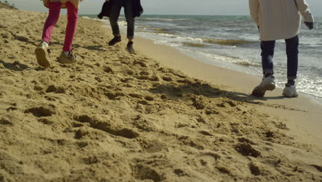 Playful-family-walking-beach-by-sea-sand.-Excited-people-legs-run-around-outside