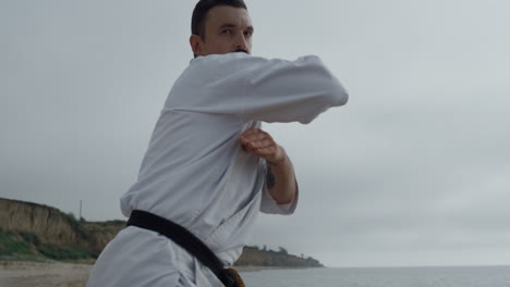 Sportsman-practicing-hands-punches-on-gloomy-beach.-Focused-man-workout-karate.