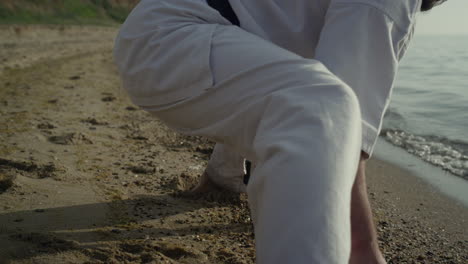 Flexible-athletic-man-stretching-on-sand-close-up.-Karate-fighter-exercising.