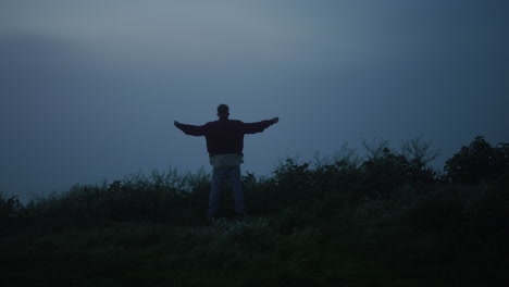 Lonely-guy-walking-in-misty-field.-Back-view-man-raising-hands-in-air