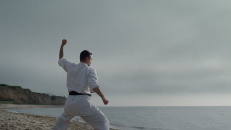 Luchador-De-Karate-Entrenando-Fuerza-En-La-Playa.-Hombre-De-Pie-En-Posición-De-Lucha.