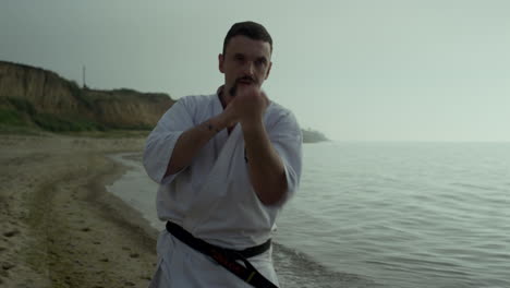 Strong-fighter-exercising-punches-on-beach-close-up.-Athlete-practicing-karate.