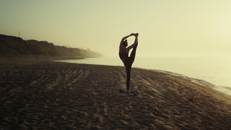 Unknown-girl-standing-twine-on-sandy-beach.-Flexible-woman-doing-stretching.