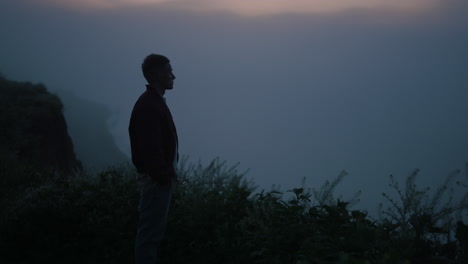 Relaxed-guy-looking-mountain-horizon-in-morning-fog.-Man-standing-on-cliff