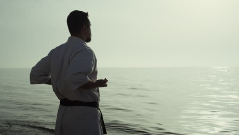 Athletic-man-honing-karate-technique-enjoying-sunset-on-beach-back-view