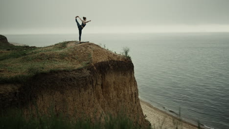 Athlete-woman-streching-holding-leg-on-beach-hill.-Girl-practicing-yoga-near-sea
