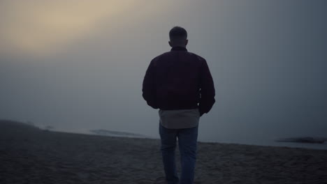 Young-man-walking-on-sandy-beach-in-morning-fog.-Lonely-guy-looking-sea-horizon
