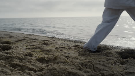 Closeup-man-feet-stepping-on-sand-training-karate.-Athlete-exercising-on-beach.
