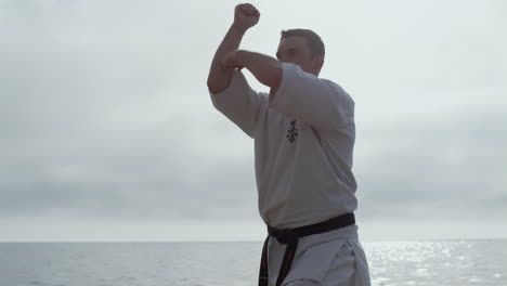 Focused-athlete-exercising-karate-on-beach-closeup.-Man-training-fighting-skills