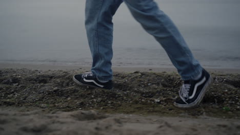 Casual-sneakers-walking-on-sea-shore-closeup.-Man-feet-enjoying-walk-on-beach