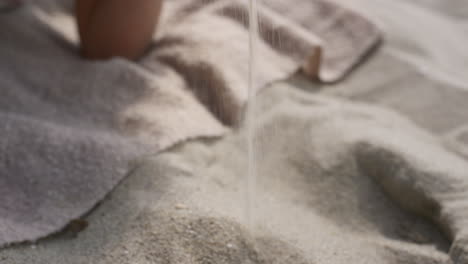 Smiling-woman-pouring-sand-between-fingers-lying-on-summer-beach-close-up.