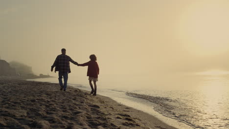 Happy-woman-and-man-walking-on-sea-beach.-Lovely-couple-holding-hands-at-sunrise