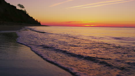 Ruhige-Meeresküste-Mit-Berghügelsilhouette-Bei-Leuchtend-Orangefarbenem-Sonnenuntergang