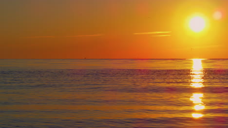 Tranquil-view-of-orange-sun-reflecting-in-clear-blue-ocean-water-in-on-sunset.
