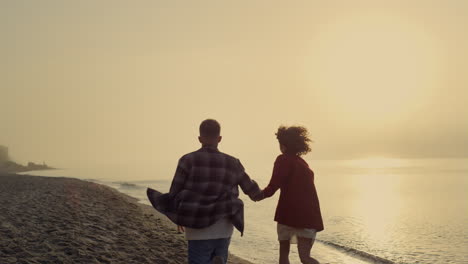 Loving-couple-running-on-sandy-beach-at-sunrise.-Girl-and-guy-dancing-at-sea
