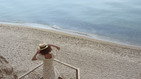 Joyful-woman-spinning-holding-straw-hat-on-wooden-ladder-seashore-sunny-day.