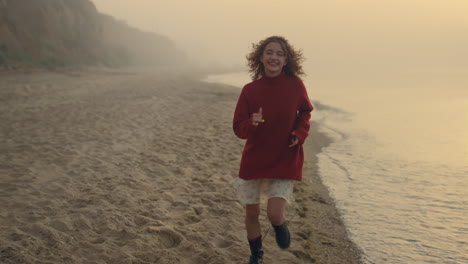 Happy-woman-running-on-sea-beach-at-sunrise.-Playful-girl-smiling-at-camera