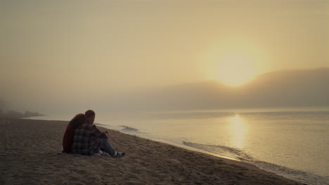 Loving-couple-sitting-on-sandy-beach-at-ocean.-Young-lovers-talking-together