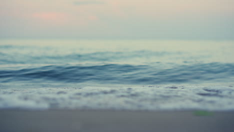 Closeup-blue-sea-waves-splashing-coastline-sand-beach-in-slow-motion-at-pink-sky