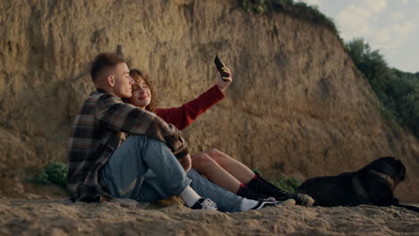 Paar-Macht-Selfie-Foto-Am-Strand-Bei-Sonnenuntergang-Mit-Dem-Smartphone.-Glückliche-Liebhaber-Mit-Hund