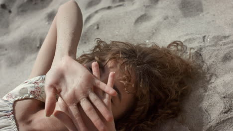 Seductive-lady-lying-beach-sand-hiding-face-behind-hands-closeup.-Woman-smiling
