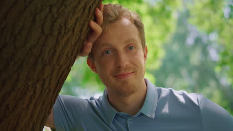 Portrait-of-man-lean-on-tree-in-park-closeup.-Handsome-guy-looking-on-camera.