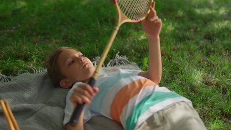 Upset-little-boy-lying-blanket-in-park.-Kid-examining-badminton-racket-net