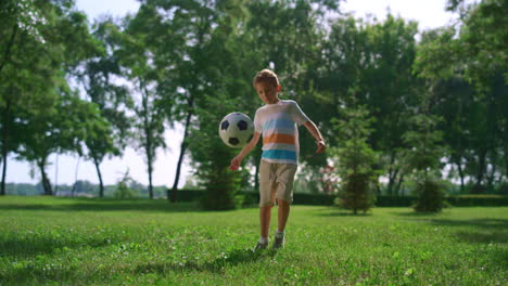 Sporty-boy-make-football-exercise-in-park.-Young-athlete-kick-ball-on-sunny-lawn