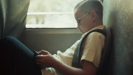 School-boy-using-gadget-playing-games-in-school-bus.-Child-sitting-at-bus-window