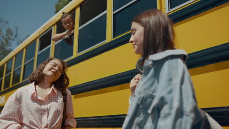 Two-cheerful-girls-talking-at-school-bus.-Schoolboy-looking-out-bus-window.