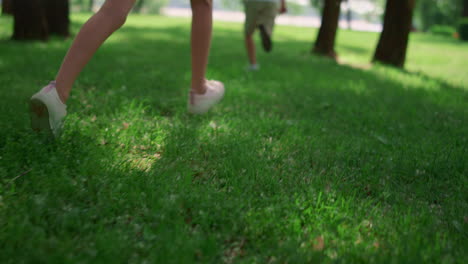 Running-children-legs-on-green-grass-meadow.-Unknown-kids-play-jogging-outdoors.
