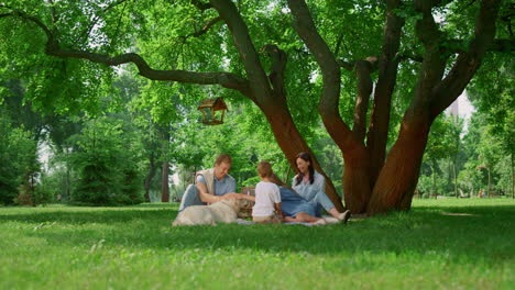 Ruhende-Familie-Mit-Hund-Beim-Picknick.-Fröhliche-Menschen,-Die-Sich-Draußen-Auf-Grünem-Gras-Entspannen