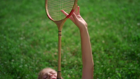 Closeup-badminton-racket-in-hands-of-smiling-joyful-girl-lying-on-blanket.