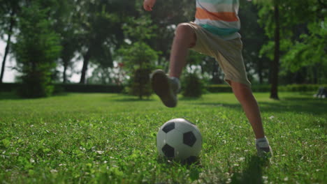 Happy-boy-play-football-on-sunlight-in-park.-Kid-make-soccer-exercise-on-nature.