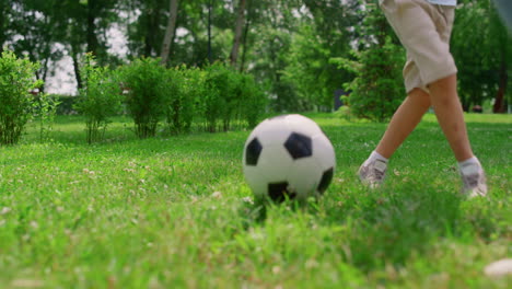 Unknown-boy-legs-making-soccer-exercise-closeup.-Son-training-football-with-dad.
