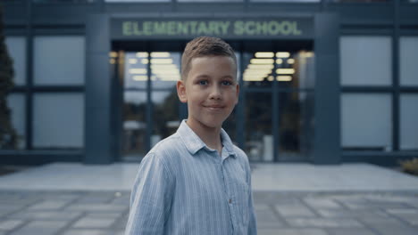 Smiling-elementary-age-boy-standing-at-school-entrance-close-up.-Portrait-pupil.