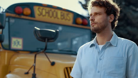 Portrait-car-driver-stand-near-yellow-school-bus.-Serious-man-looking-camera.