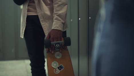 Boy-hand-holding-skateboard-with-stickers-in-school-hall-close-up.-Hobby-concept