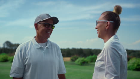 Two-golf-players-discuss-golfing-game-at-fairway.-Happy-couple-chat-on-sunny-day
