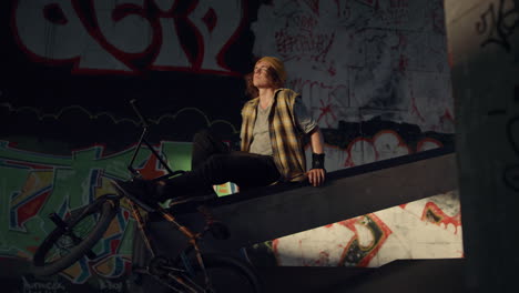 Calm-millennial-man-relaxing-with-bmx-bike-at-sun-rays-near-graffiti-wall.