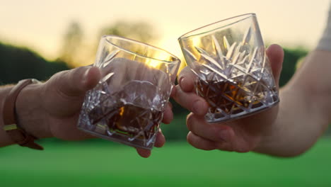 Friends-toast-glasses-outdoors.-Two-men-clinking-drinks-together-on-sunset-field