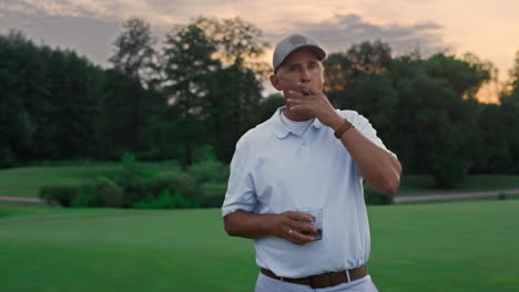 Wealthy-elderly-smoke-cigar-on-golf-field.-Old-guy-posing-looking-camera-outside