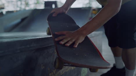 Skateboarder-holding-skate-board-in-hands-at-skate-park.-Man-hands-skateboard.