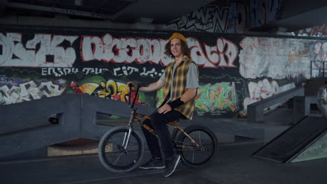 Positive-man-having-break-after-training-on-bmx-bike-at-skate-park-graffiti.